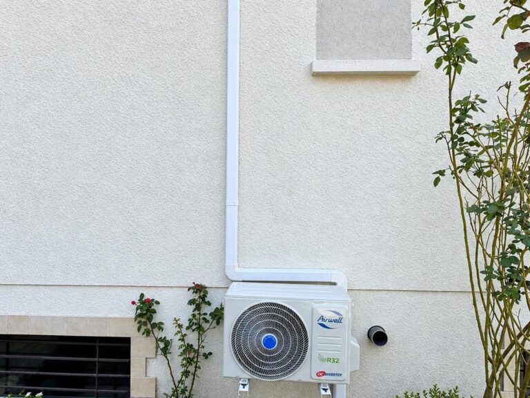 Unité extérieure Airwell R32 DC Inverter murale au-dessus d'un massif avec rosier