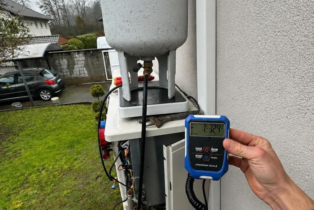 Technicien contrôlant la charge en fluide frigorigène d'une pompe à chaleur avec une balance de charge électronique