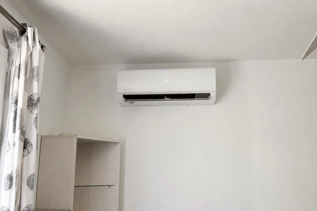 Unité intérieure de climatisation réversible fixée en haut du mur d'une chambre, à côté d'une fenêtre