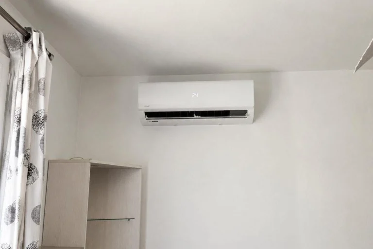 Unité intérieure de climatisation réversible fixée en haut du mur d'une chambre, à côté d'une fenêtre
